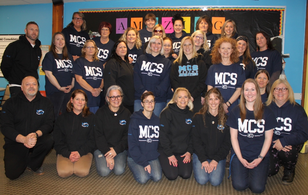 School teachers and staff pose for a group photograph all wearing tops with the school logo on the front.