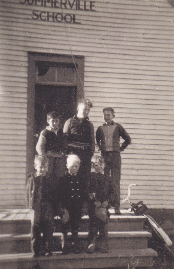 Six young boys pose on the stairs of a school. A bicycle leans against the side of stairs to the right .