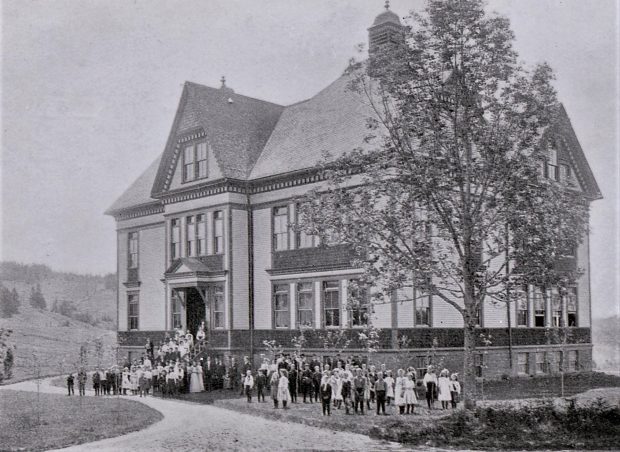 The school with students and staff standing on the front steps and lawn.