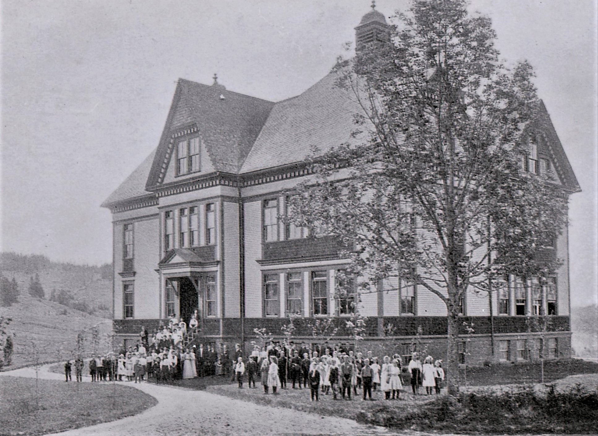 The school with students and staff standing on the front steps and lawn.