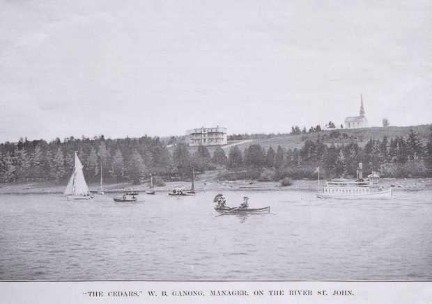 Circa 1900, three story hotel close to the river shore and a church with a spire on the hill behind. People in canoes, sailboats and a steamboat on the water in foreground.