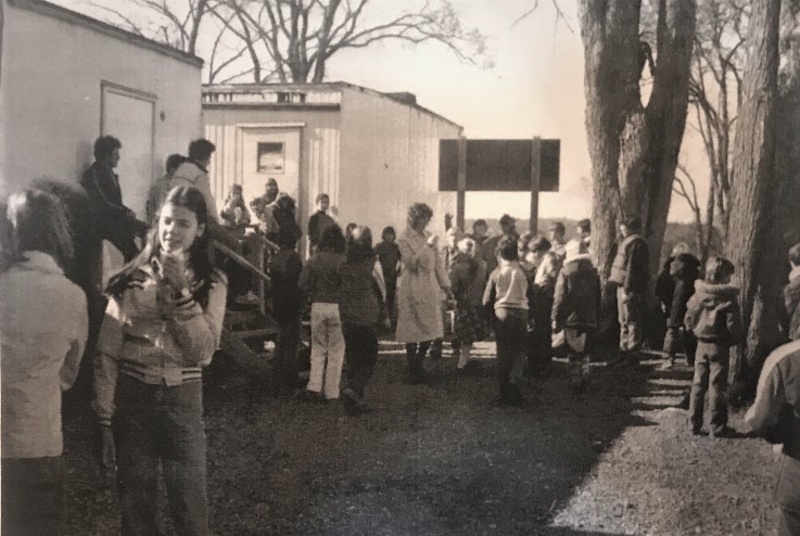 Plusieurs élèves et un enseignant font une pause sur les marches et à l’avant de deux salles de classe mobiles. 