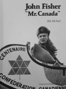 Un homme portant un chapeau de fourrure avec une queue pose à la proue d’un canot qui affiche le logo du centenaire de la Confédération canadienne. 