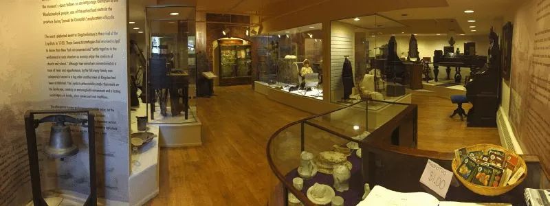 JFMM artifacts on display including a brass bell, china, clothing, piano and other furnishings.