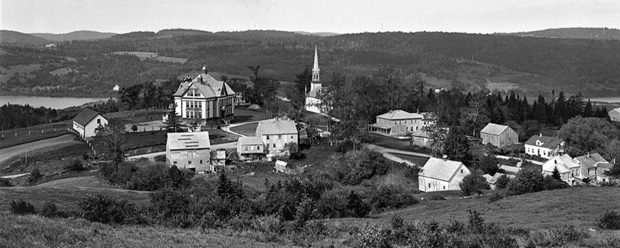 Aerial view of Kingston shows historic MCS , Trinity Church and village buildings set in rolling hills with Bates Lake in the background on the left and Kingston Creek on the right.