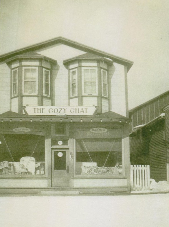 Black and white photograph. Exterior view of Cozy Chat. There are two bay windows on the second floor.