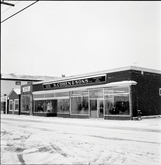 Black and white archival photograph. Street view. S. Cohen & Sons and Cohen’s Furniture Department looking west on Main Street, Windsor. Sign above store reads: DRY GOODS; HARDWARE; FURNITURE; S. COHEN & SONS LTD.; WHOLESALE AND RETAIL. Female and male manikins visible in the store windows.