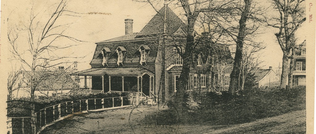 A black-and-white postcard showing a large elegant house with a veranda, bay window, and mansard roof. A few mature trees line the drive to the house.