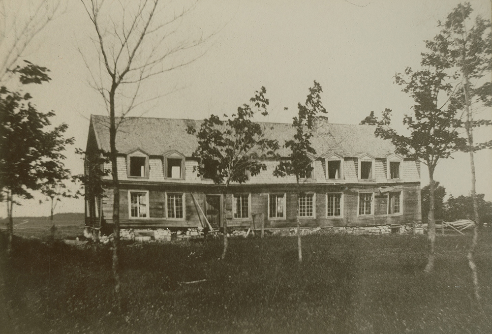 Photo noir et blanc. Longue maison abandonnée. Le toit mansardé est percé de nombreuses lucarnes.