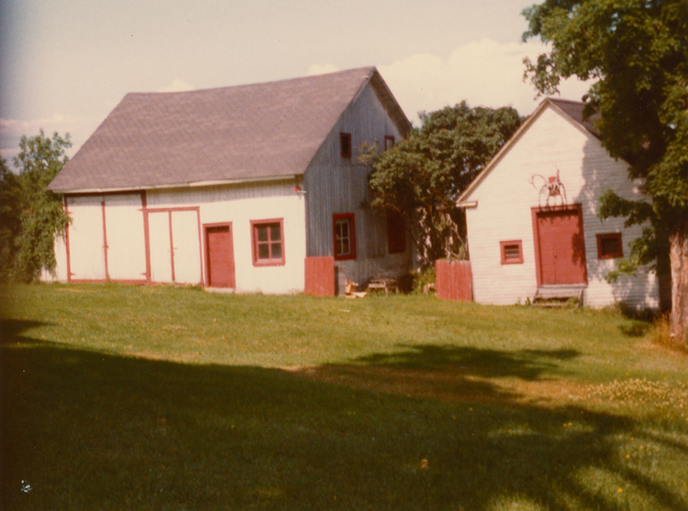 Colour photograph of two wooden buildings painted white. The doors and window frames are painted red.
