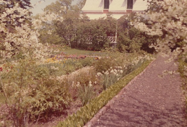 Colour photograph of the gardens of the Manoir in bloom, with many trees.