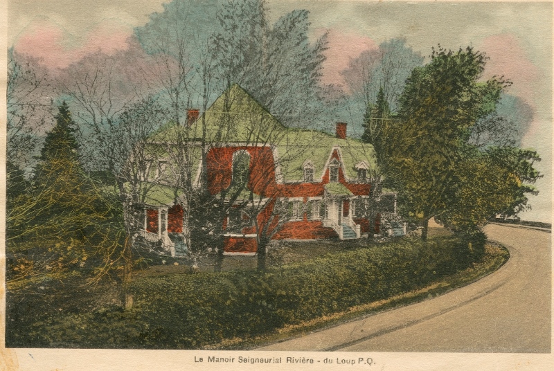 Colour image of a large brick house in winter behind a low cedar hedge and several trees.
