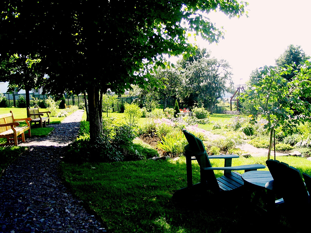 Colour photograph of the gardens of the Manoir in bloom, with many trees.