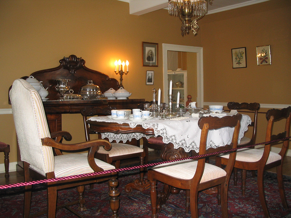 Colour photograph of a table with porcelain dishware and silverware. An imposing sideboard is in the background.