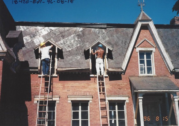 Colour photograph of workers on ladders repairing the dormer windows of Manoir Fraser.