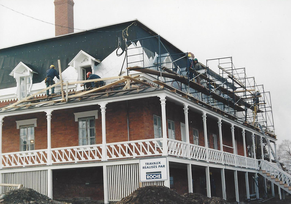 Colour photograph of workers applying a new covering to the mansard roof.