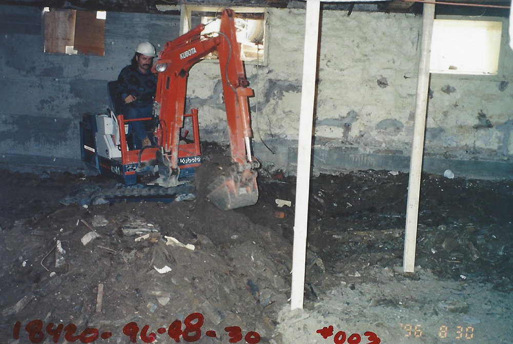 Colour photograph of a worker excavating the basement of Manoir Fraser with a mechanical shovel.
