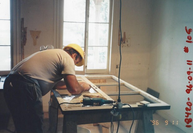 Colour photograph. Inside the manor, a man restores a window.