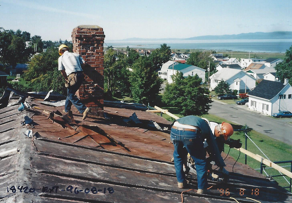 Colour photograph of workers repairing the roof. Houses and the river can be seen in the background.