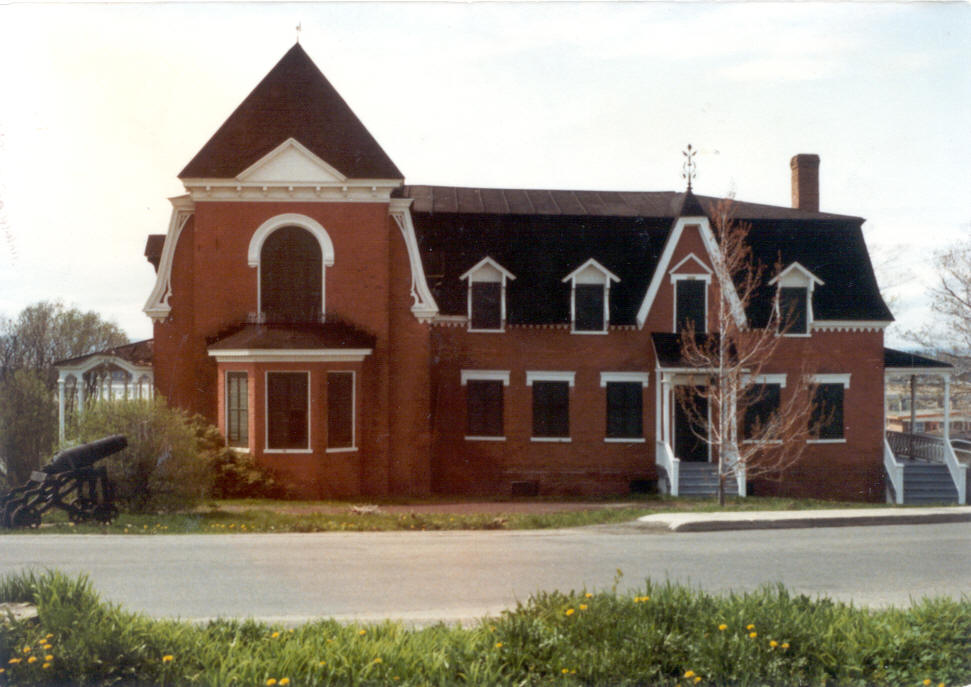 Colour photograph of a vacant house with a brick façade. All the wooden shutters are closed.