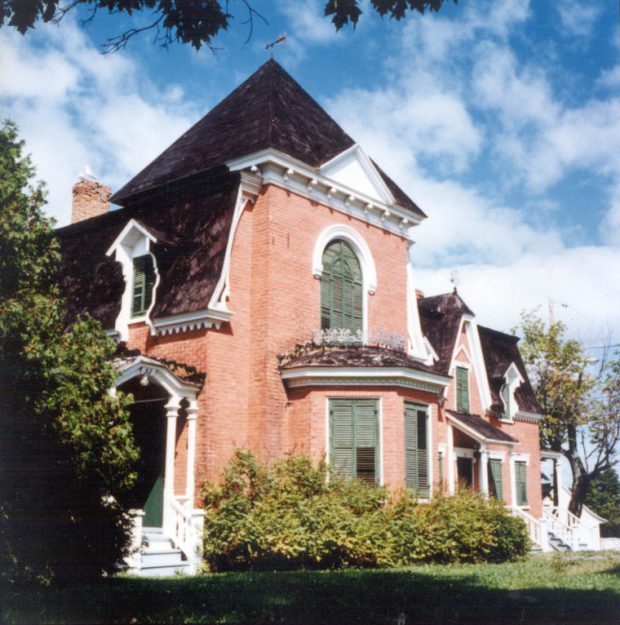 Colour photograph of a brick house with closed shutters.