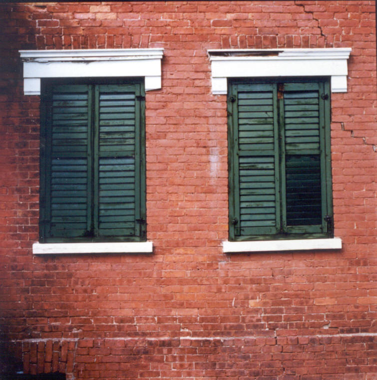Close-up colour photograpĥ of two windows in a brick house with closed shutters.