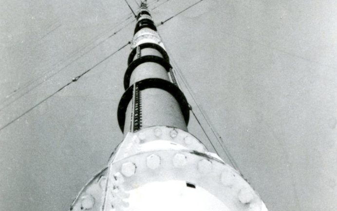 A radio tower, as seen when looking from its base straight up to the top. A series of support wires extend outward in four directions.