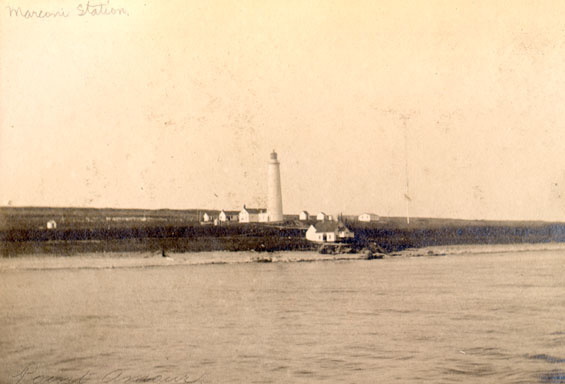 A lighthouse and several small buildings on a low coastline.