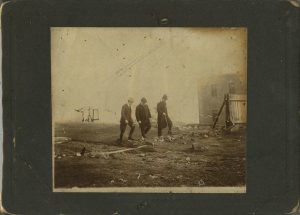 Three men in suits and hats walk together across a hilltop of low grass and rock.