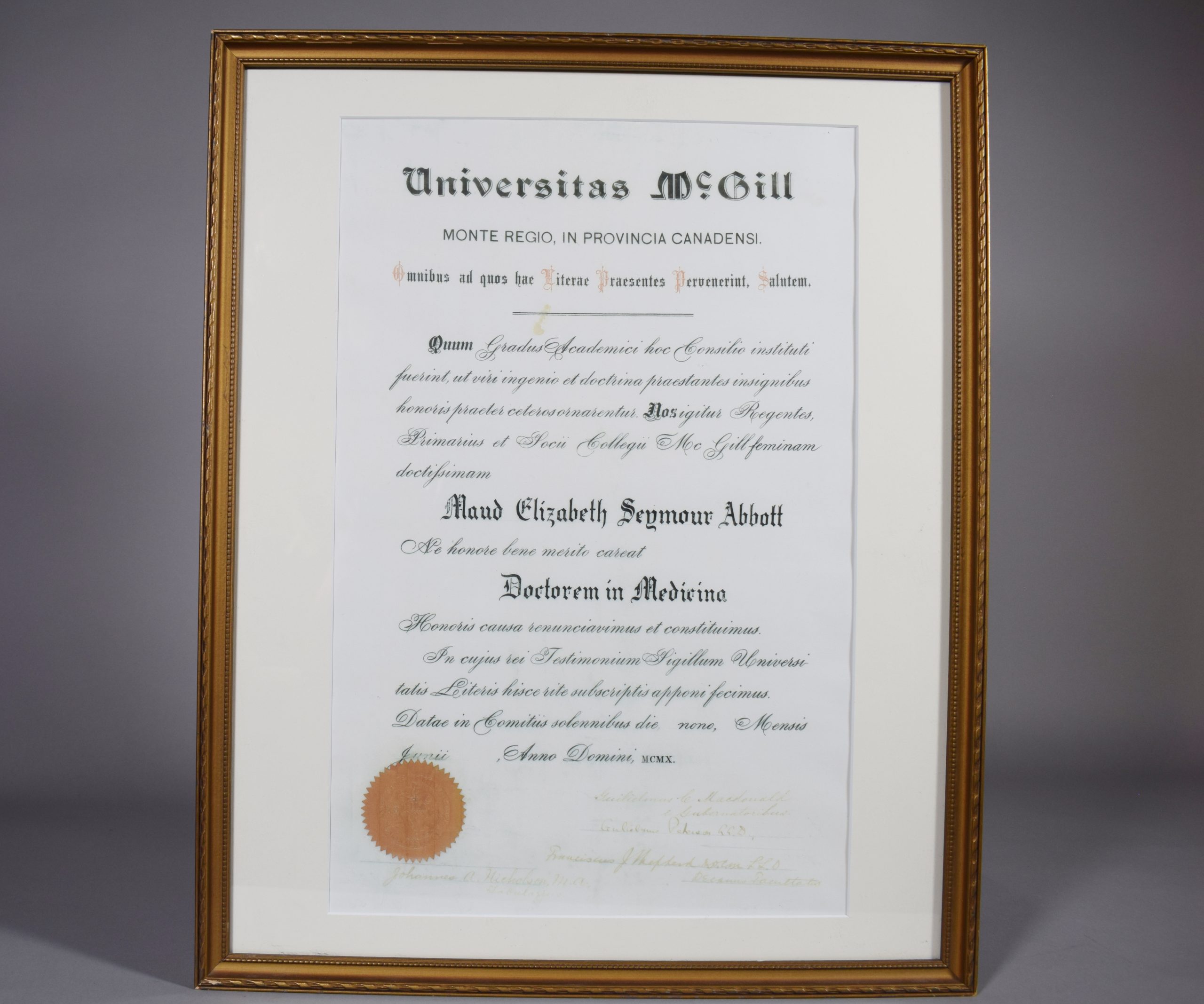 McGill University diploma. “Doctorem in Medicina” awarded to Maud Elizabeth Seymour Abbott by McGill University. The text on the diploma is in Latin. The lower left corner bears the red seal of McGill University, with several signatures to its right. The diploma is displayed in a narrow, simply decorated gold frame with a white mat.