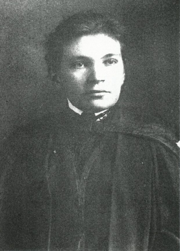 Front of a black and white postcard showing a portrait of Maude Abbott as a young adult, from the waist up. She is wearing a dark graduation gown. Her dark hair is tied behind her head and she is looking slightly to the left.