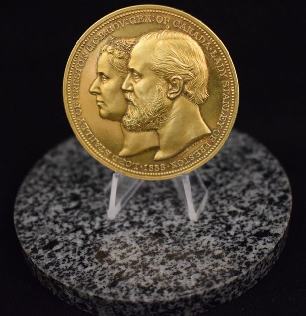 Colour photograph of the Lord Stanley Gold Medal awarded to Maude Abbott in 1888, front face. The medal is gold in colour and shows, in the centre, the jugate portraits of Lord Stanley of Preston and his wife, Lady Stanley of Preston. Around their portraits circles the inscription “Lady Stanley of Preston 1888 Lord Stanley of Preston G.C.B. Gov. Gen. Of Canada”.