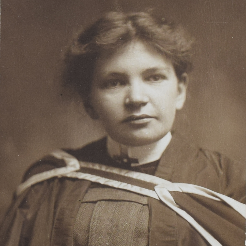 Black and white photograph of Maude Abbott as a young adult, from the waist up. She is wearing a graduation gown. Her dark hair is tied behind her head and she is looking slightly to her left.