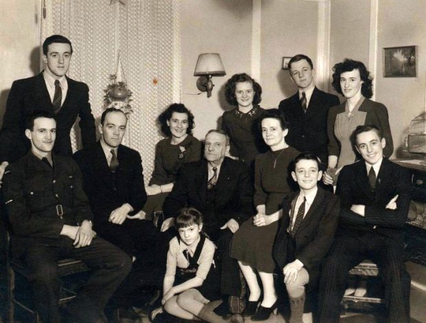 Black and white photograph of Hélène B.-Beauséjour, her husband and her 10 children. B.-Beauséjour and her husband are in the middle of the photograph. One of their sons is sitting on their immediate left, and three others are posing on their right. Three daughters and one son are behind them. Two more of their children, a son and a daughter, are sitting on the floor in front of them.