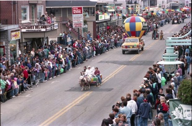 Photograph of a parade organized as part of the Louiseville Buckwheat Pancake Festival. A float pulled by a pony is making its way down the town’s main thoroughfare. People are looking on from either side of the street.