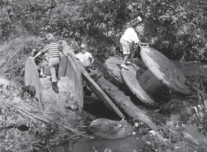 Black and white photograph of children playing on equipment left behind by a since-closed industrial operation. The photograph was taken during a clean-up effort along the banks of the Champlain River in August 1989.