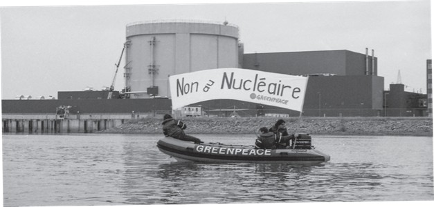 Black and white photograph of three Greenpeace activists in an inflatable boat on the St. Lawrence River, in front of the Gentilly-2 Nuclear Generating Station. They are holding up a banner with the words “No to Nuclear.”