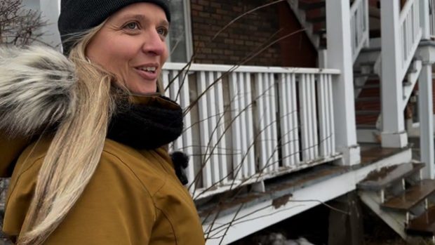 Colour photograph of Paule Vermot-Desroches, dressed in a yellow winter coat and a toque, in front of an apartment building balcony.