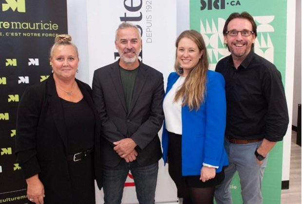 Colour photograph showing four people, two men and two women, standing in front of promotional banners for different organizations.