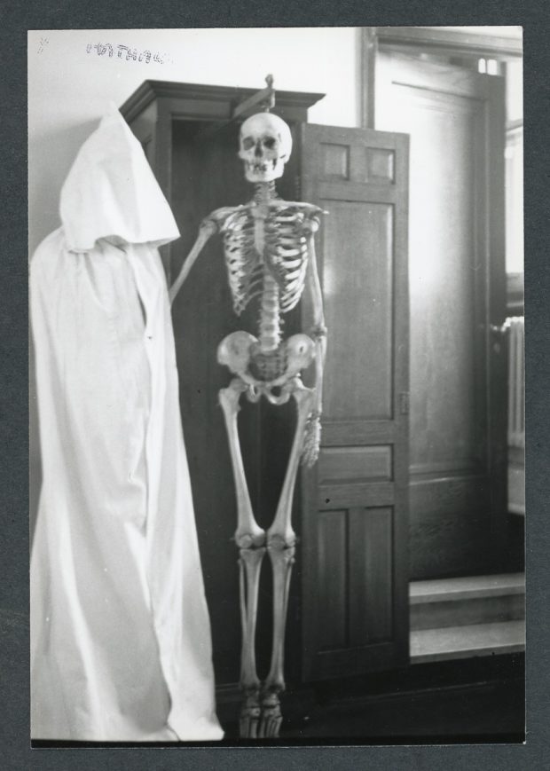 Black and white photo of a human skeleton displayed in a wooden cabinet.