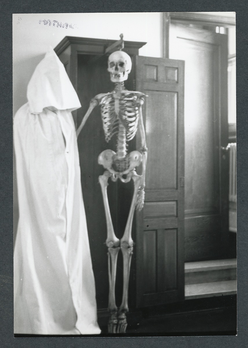 Black and white photo of a human skeleton displayed in a wooden cabinet.