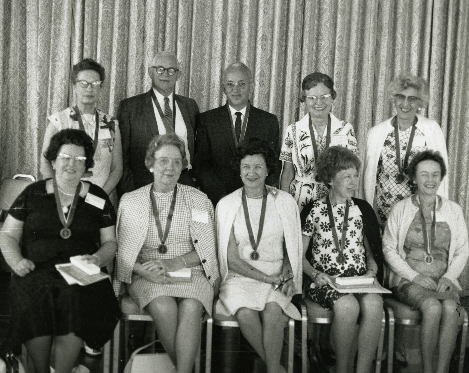 Black and white photo of 8 women and 2 men posing shoulder to shoulder, wearing medals.