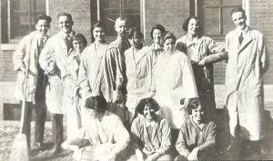 Black and white group photo of students of all genders posing in rows, wearing lab coats.