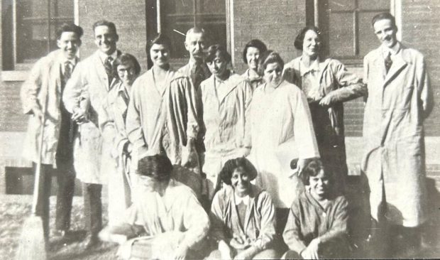 Black and white group photo of students of all genders posing in rows, wearing lab coats.