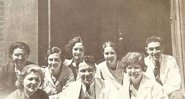 Black and white group photo of students of all genders posing in two rows, wearing lab coats. Photo is cropped above the shoulders.