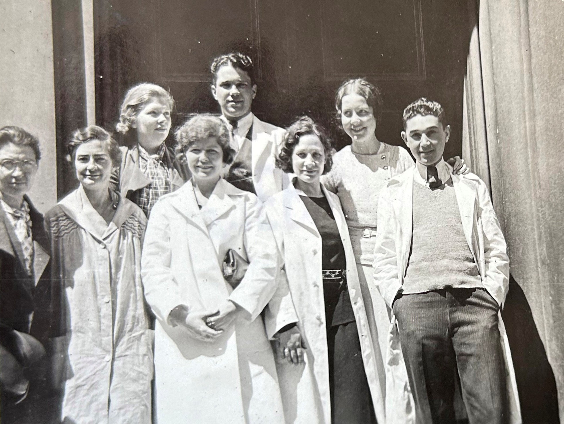 Black and white photo of eight classmates posing in two rows wearing their lab coats.