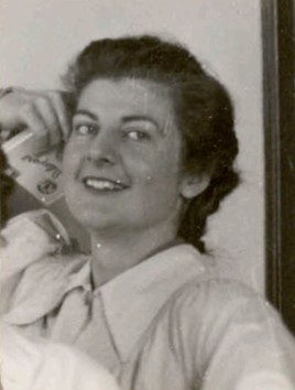Black and white photo of a woman posing with her hand held to her head and smiling at the camera. She is holding what looks like a cigarette carse.
