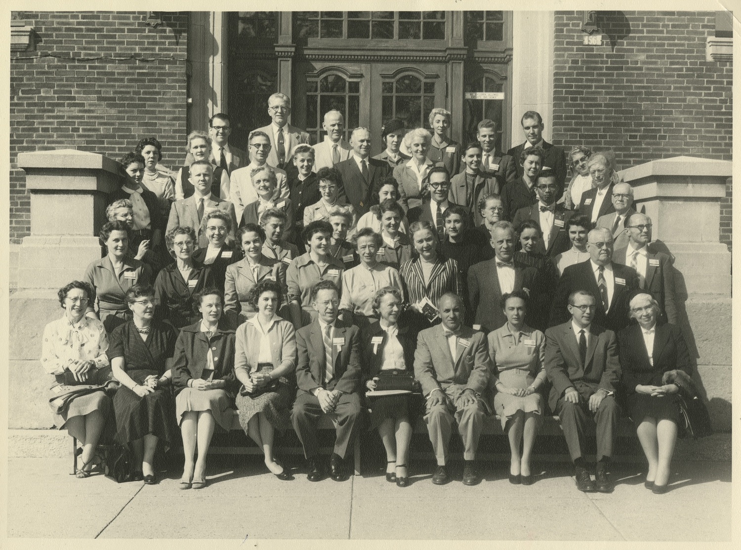 Black and white photo of a large group of people posing on the steps of a brick building.