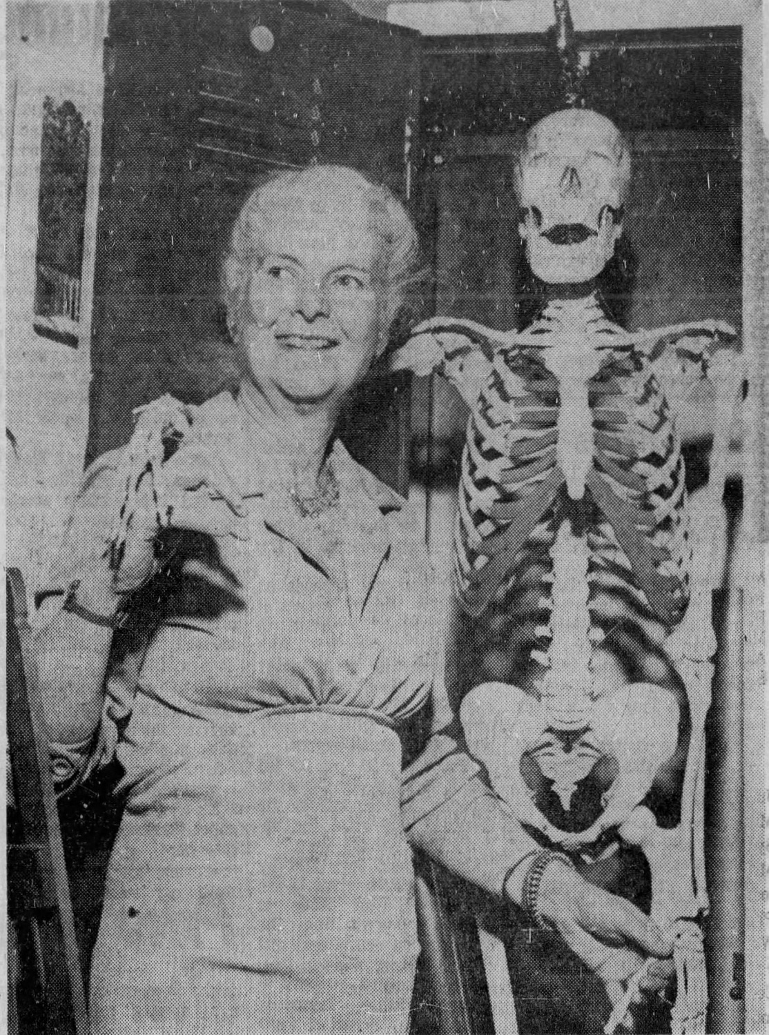 Black and white photo of Mary Gzowski standing next to a skeleton with its arm draped over her shoulders.