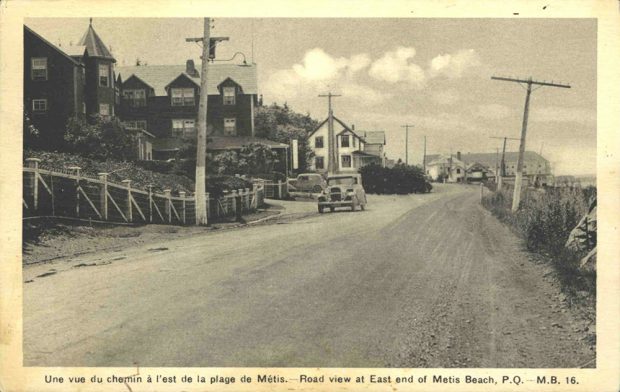Black and white postcard printed on card presents the Chemin du Roi. The dirt road crossing the town of Métis-sur-Mer. A car is parked along the road. Along the way there are 2 of the major hotels of the time as well as some of the magnificent summer residences.